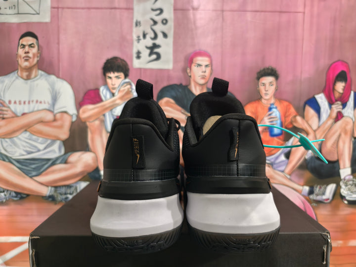 Rear view of black and white Nike basketball sneakers with gold heel branding on a black box.