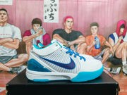 Side profile of a white basketball sneaker with blue Swoosh detailing, blue laces, turquoise outsole accents, and a translucent blue heel section.