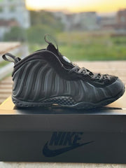 All-black high-top Foamposite-style sneaker photographed on a Nike shoebox.