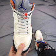 Front view of the white sneaker showing the tongue logo, white laces, lace toggle, and black toe trim.