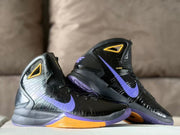 Two black Nike high-top basketball shoes with purple Swooshes and gold sole accents