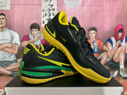 Angled view showing the black textured upper, lace-up closure, green side detail, and yellow outsole.