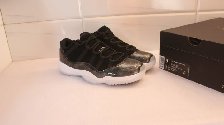 Pair of black and dark metallic Jordan low-top sneakers beside a black shoebox.