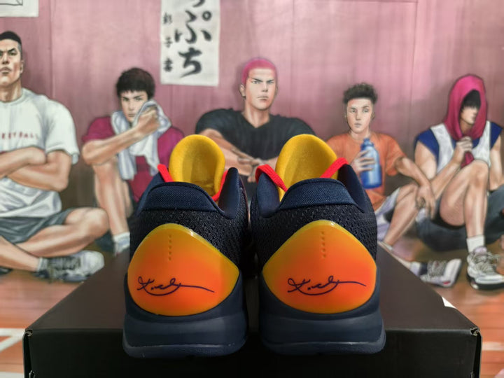 Rear view of dark blue basketball sneakers with bright orange heel panels, gold collars, and black outsoles on a shoebox.