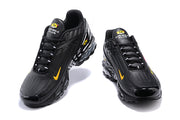 Front views of black Nike Air Max Plus sneakers with yellow accents and lace-up closures.