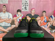 Front view of the sneaker pair showing black laces, black uppers, yellow tongue accents, and green toe outsoles.