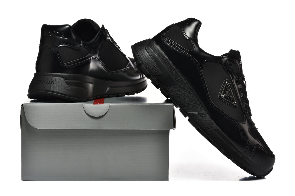 Pair of black Prada-branded sneakers shown from the side with a shoebox