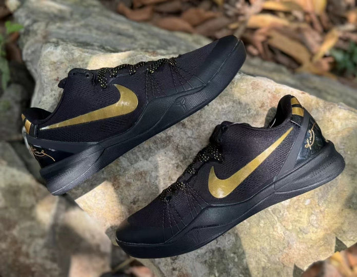Pair of black and gold Nike Kobe 8 sneakers shown from an angled side view on rocks.