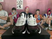 Front view of the white and black basketball-style sneakers showing white laces, padded tongues, glossy black toe panels, and Jumpman-style logos.