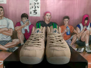Front view of the beige sneakers showing tonal laces, padded tongues, green pull tabs, and patterned upper accents.