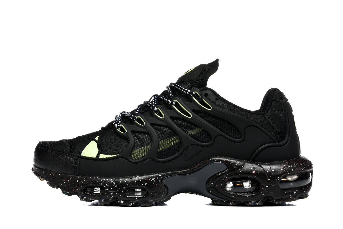 Side view of black Nike Air Max Plus Utility sneakers with neon green accents, patterned laces, and a speckled sole.