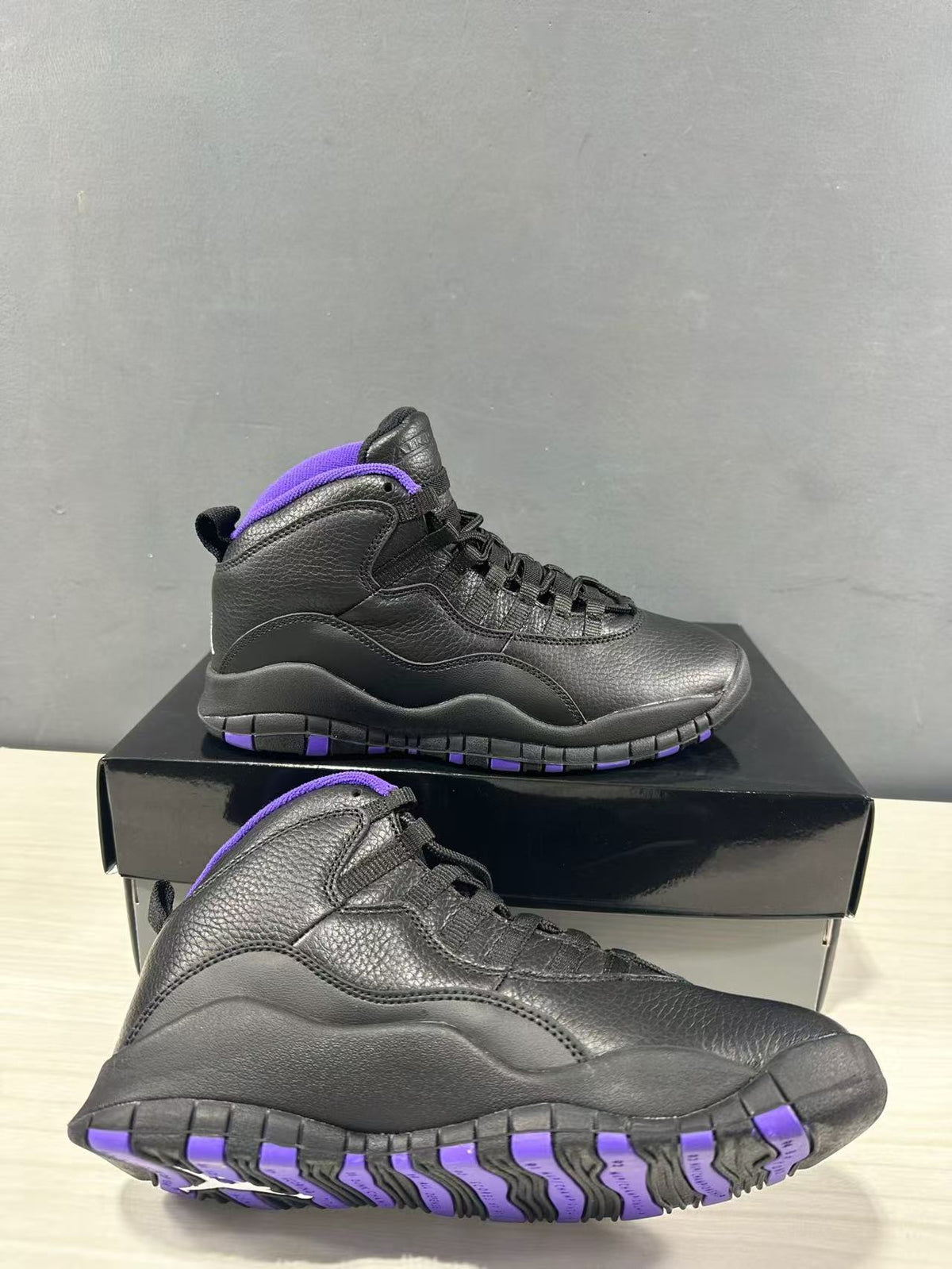 Pair of black high-top Jordan sneakers with purple collar and outsole accents, shown on a black shoebox.