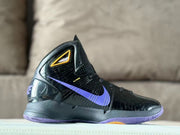 Side profile of a black Nike basketball shoe with purple Swoosh and gold ankle detail