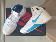 Overhead view of the sneakers resting on a Nike-branded box, showing the blue Swoosh and outsole details.