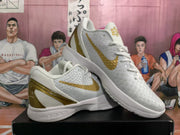 Angled view of paired white Nike basketball sneakers with gold Swoosh details and translucent gold heel accents.