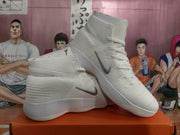 Angled view of a pair of white and silver Nike high-top basketball sneakers displaying the side Swooshes and layered soles.
