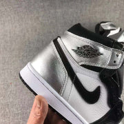 Side close-up showing the metallic silver heel panel, white side panel, black Swoosh-style detail, and winged ankle logo.
