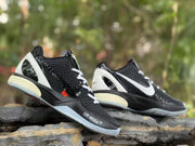 Angled outdoor view of the black sneaker pair showing white heel panels, textured uppers, and contrasting side branding.