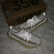 Flash-lit view of reflective-looking cream and gray sneakers placed in front of a Yeezy 350 shoebox.