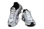 Pair of silver Nike Shox TL sneakers viewed from the front, showing the laces and column-shaped soles.