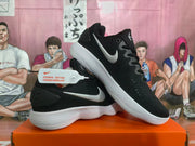 Side view of black Nike sneakers with silver side logos, black laces, and white ridged soles.