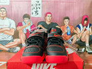 Front view of the black and red high-top sneakers showing laces, perforated toe panels, red stitching, and ankle straps.