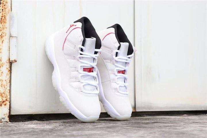 Pair of predominantly white Air Jordan 11 sneakers with red accents and black collars.