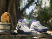 Outdoor three-quarter view of two white and purple high-top sneakers displayed on a log.