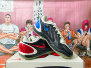 Nike basketball shoes shown at an angle, with black and white uppers, blue and red accents, and translucent outsoles.