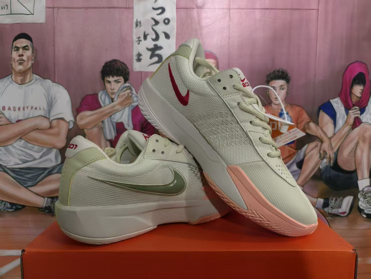 Pair of light olive Nike basketball sneakers shown at an angle, with red Swoosh details and pink-toned outsoles.