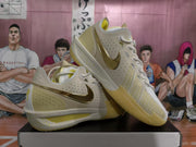 Angled view of Nike basketball sneakers showing perforated panels, metallic gold Swooshes, and yellow outsole