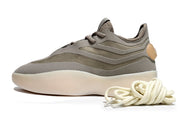 Side view of a brown-gray low-top lace-up sneaker with layered panels, cream outsole, and coiled laces.