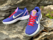 Top and angled view of the sneakers showing the purple tongue, gold Kobe emblem, red laces, and patterned upper.
