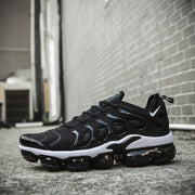 Black and white Nike TN-10 sneaker resting outdoors against a brick wall.
