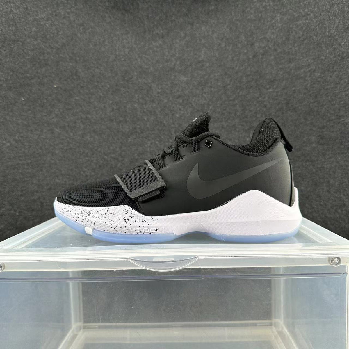 Side view of a black Nike basketball shoe with a forefoot strap, white speckled midsole, and light blue outsole.