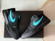 Top-down angled view of both sneakers on a black box, highlighting the turquoise logos, textured black panels, and heel graphics.