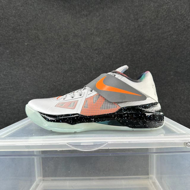 Side view of a white and gray Nike basketball sneaker with orange accents, a midfoot strap, black speckled midsole section, and translucent-looking outsole.