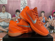 Angled view of orange Nike basketball sneakers with textured uppers, orange laces, silver Swoosh branding, and Zoom lettering on the midsole.