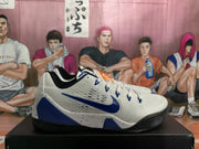 Side view of a white Nike basketball sneaker with a blue Swoosh, blue heel panel, perforated upper and black outsole.