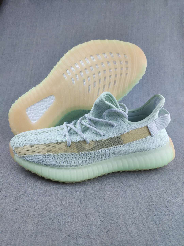 Pair of pale green and beige Yeezy 350 V2 sneakers shown from the side and underside.