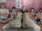 Front view of beige sneakers with tonal laces and textured uppers on a shoebox.