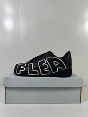 Side view of a black low-top sneaker with large outlined FLEA lettering in black and white.