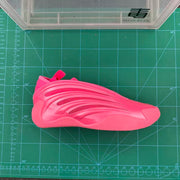 Vivid pink sneaker displayed side-on over a cutting mat, showing its sculpted upper and textured sole.