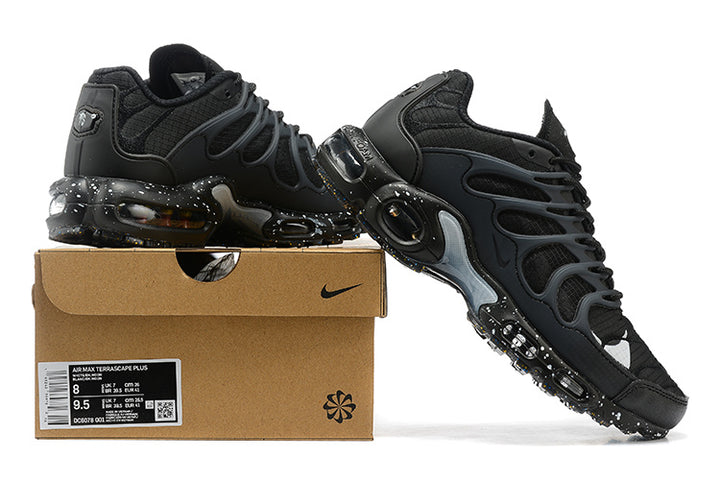 Black Nike Air Max Plus sneakers displayed on a shoe box, showing the side profile and speckled sole.