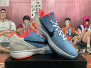 Three-quarter view of the blue-grey basketball sneakers showing the textured upper, black Swoosh, white laces, and orange-red outsole accents.