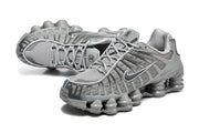 Angled view of a pair of grey Nike Shox TL sneakers showing the laces, mesh panels and segmented cushioning columns.