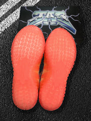 Close-up of the pair's translucent orange outsoles with repeated textured tread patterns.