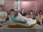 Side view of white Nike Kobe basketball shoes with teal side detailing, coral-red accents, and gum-colored outsoles