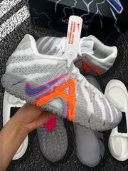 Close-up side view of a grey Nike basketball sneaker with bright orange and pink accents, textured upper, and visible outsole components.