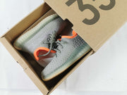 Gray and orange Yeezy 350 V2-style kids' sneakers displayed inside a cardboard shoebox.